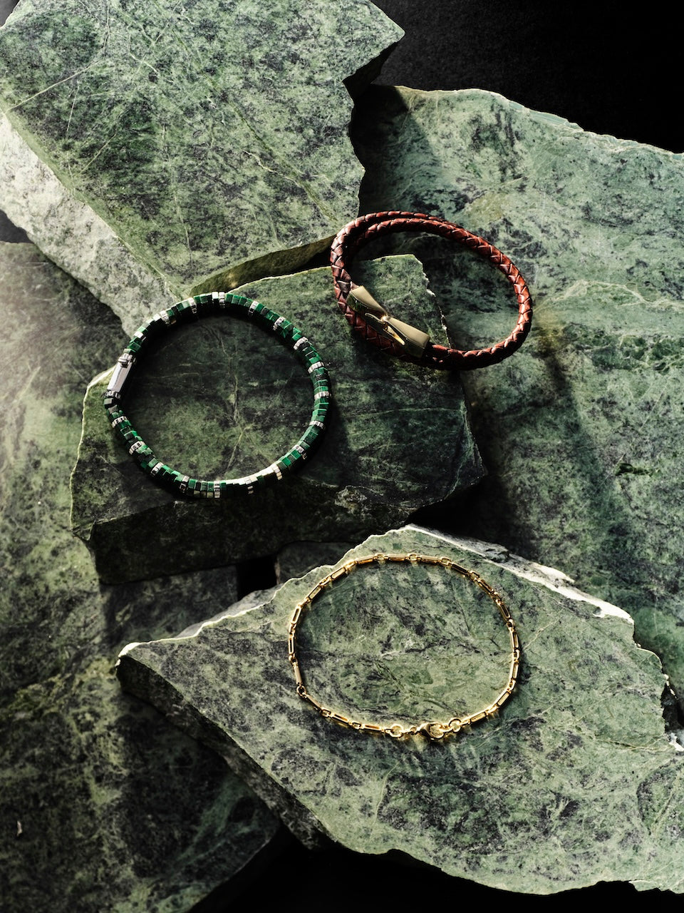 Three men's bracelets on a textured stone surface