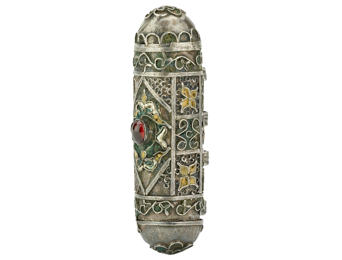 An ornate vintage silver-toned cylindrical amulet with intricate filigree detailing, floral enamel accents, and a central red gemstone