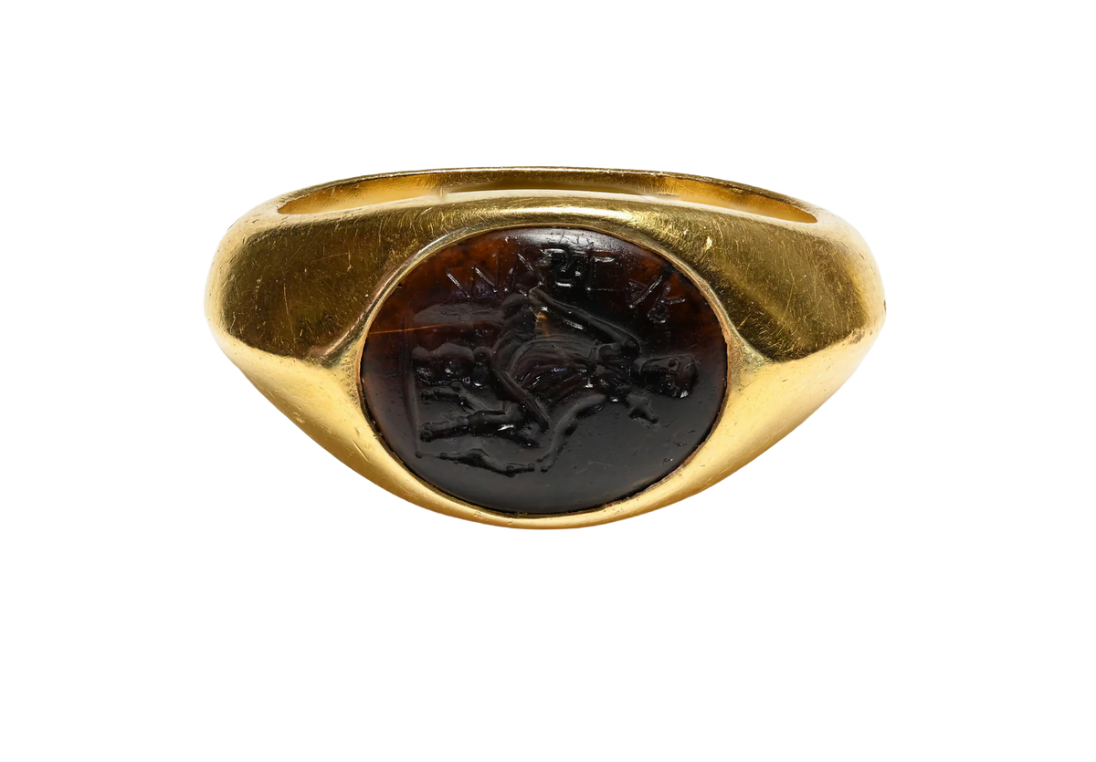 A Roman gold signet ring featuring an oval dark brown carved cabochon stone with an embossed figure, shown against a plain white background.